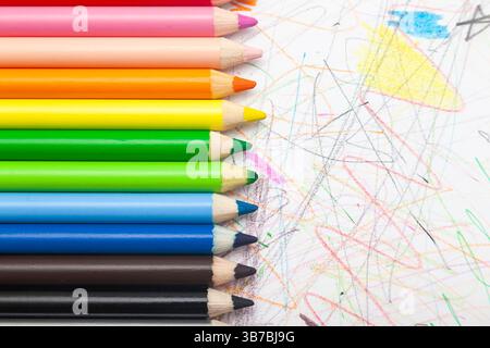 Multi-colored pencils lie on white paper drawn with multi-colored curved lines. Stock Photo