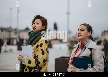 Two women outdoors holding notebooks and engaged in thoughtful conversation Stock Photo