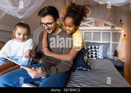 Excited single father plays with diverse, multi-ethnic daughters. Using digital tablet enjoy weekend Stock Photo