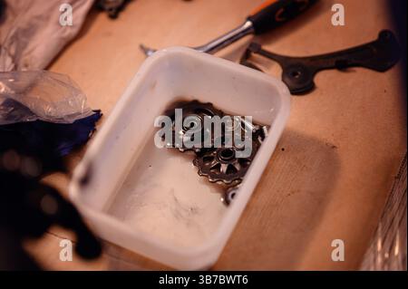Close-up of bicycle derailleur pulleys and small parts soaking in a container, surrounded by tools on a workshop table. Stock Photo