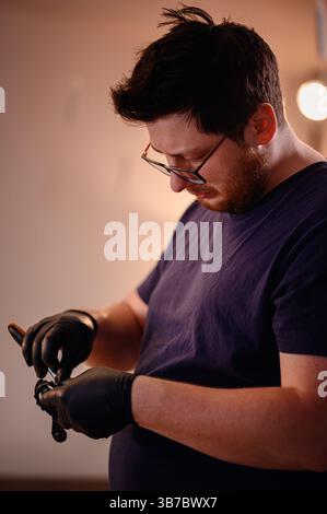 Man wearing gloves and glasses carefully works on a small bicycle part, showing concentration in a cozy indoor workspace. Stock Photo