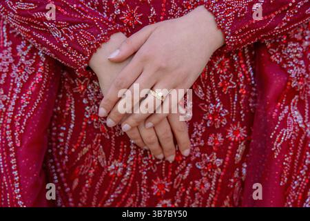 Close-up photo of a persons hands with a wedding ring resting on a beautifully embellished red dress, emphasizing craftsmanship and cultural attire Stock Photo
