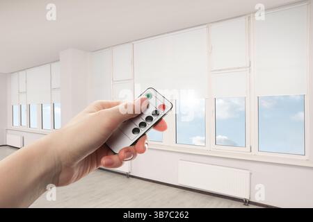 Woman using remote to control blinds in room, closeup Stock Photo