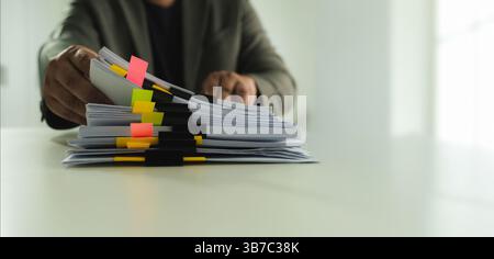 Stacks of paper files and checking document businessman checks financial documents on his laptop, managing corporate reports and legal paperwork at hi Stock Photo