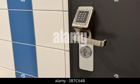 Modern electronic door lock with keypad on a dark door next to blue and white tiled wall showcasing advanced security technology. Stock Photo
