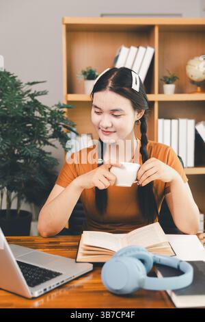woman sitting at desk working on laptop taking notes in notebook, female studying online, watching webinar using computer, writing check list. Remote Stock Photo