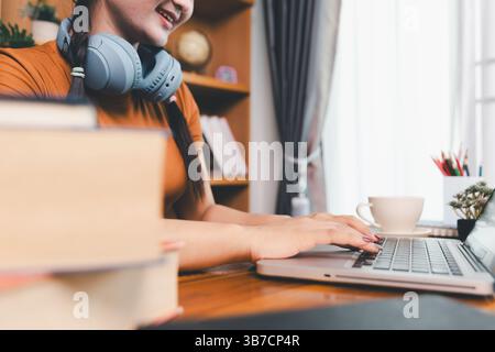 woman sitting at desk working on laptop taking notes in notebook, female studying online, watching webinar using computer, writing check list. Remote Stock Photo