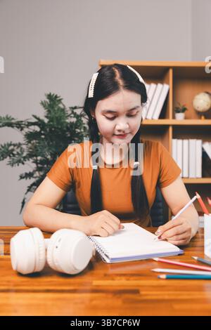 woman sitting at desk working on laptop taking notes in notebook, female studying online, watching webinar using computer, writing check list. Remote Stock Photo
