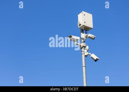A tall pole with three security cameras and a box against a clear blue sky Stock Photo