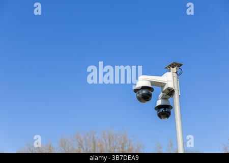 Two security cameras are mounted on a pole, watching over the area under a clear sky Stock Photo