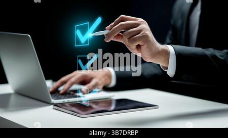 Businessman with laptop touching icon of check mark list on tablet screen. Technology innovation on a virtual screen. Concept of Compliance Stock Photo