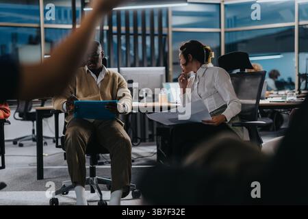 Multicultural colleagues working together on a project at night, focusing on meeting their deadline. Stock Photo