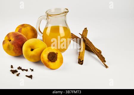 Peaches isolated in close-up with white background and copy space, accompanied by a jug of juice and some spices Stock Photo