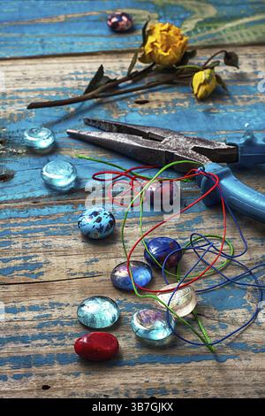 Beads, pliers, and other needlework accessories on outdated turquoise wooden background Stock Photo