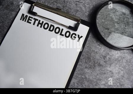 Concept of Methodology write on paperwork with a magnifier isolated on Wooden Table. Stock Photo