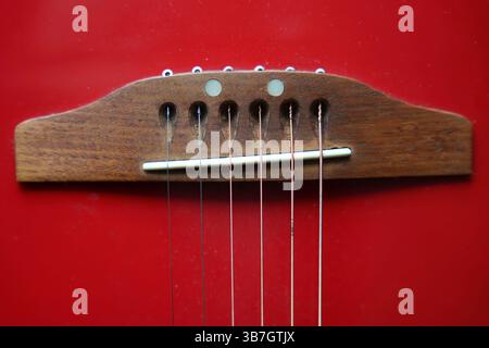 Close-up of a guitar bridge and strings on a vibrant red background, highlighting the instrument's wooden and metallic elements Stock Photo