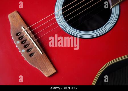 Close-up view of a red acoustic guitar highlighting its bridge, soundhole, and strings against a contrasting black background Stock Photo
