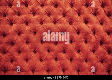 Close up background texture of scarlet red capitone genuine leather, retro Chesterfield style soft tufted furniture upholstery with deep diamond patte Stock Photo