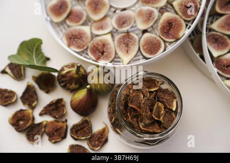 Fresh figs lie on the table next to dried figs in a glass jar and a dehydrator. Top view. Stock Photo