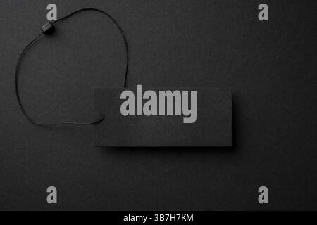 Blank black cardboard clothing tag with string on black background Stock Photo