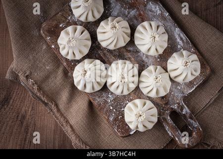 Freshly frozen khinkali, raw, on a wooden chopping board, top view, rustic style, no people Stock Photo