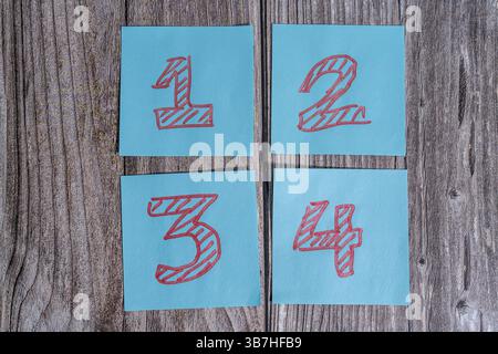 Four sticky notes with numbers one, two, three and four are laying on a wooden desk Stock Photo