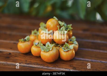Bunch of ripe orange persimmons lies on a brown wooden table. Stock Photo