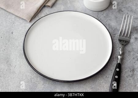 Top view of empty ceramic plate and fork on gray stone background. Minimalist rustic table setting with linen napkin. Clean space for food presentatio Stock Photo