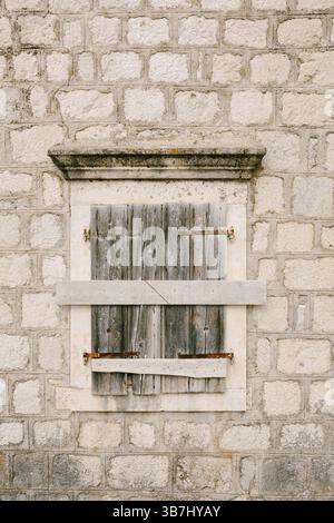 An old building with a window with closed window shutters and hammered boards. Stock Photo
