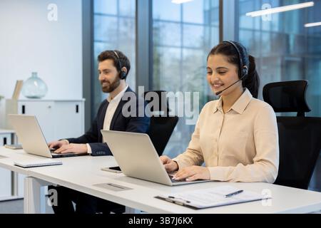 Smiling customer service representatives working in a modern office, using laptops and headsets, assisting clients professionally. Stock Photo