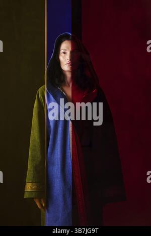 Woman in colorful traditional Asian patchwork robe standing behind the colorful glass Stock Photo
