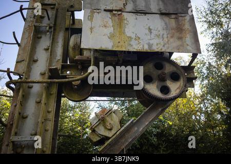 A rusted old machine with a chain and gears. The machine is leaning on a tree Stock Photo