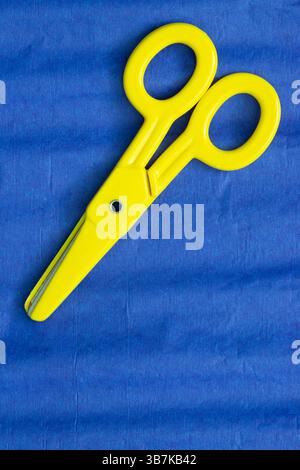 Blue crepe tissue craft paper background with yellow childrens scissors. Craft hobby material concept. Stock Photo