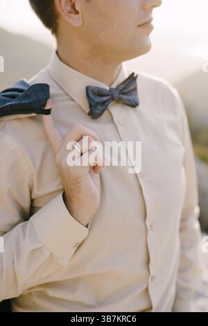 Groom in a beige shirt and bow tie holds his jacket on his shoulder with his finger. Close-up. Stock Photo