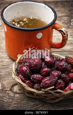 Old iron mug of tea and dried berries of the wild rose on wooden table Stock Photo