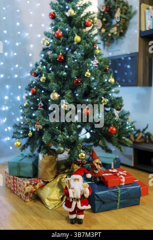 Santa and elves figurines near colorful gifts lying on the floor under the Christmas tree. Stock Photo
