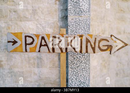 Wooden pointer with an arrow near the stone wall. Caption: Parking. Stock Photo