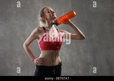 Happy young woman cooling off after intense workout, pouring water from bottle on neck, feeling refreshed. Stock Photo