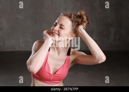 Tired young woman in sports bra feeling neck pain after fitness workout, massaging sore muscles and smiling. Stock Photo