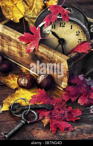 Obsolete alarm clock on wooden background strewn with fallen leaves Stock Photo