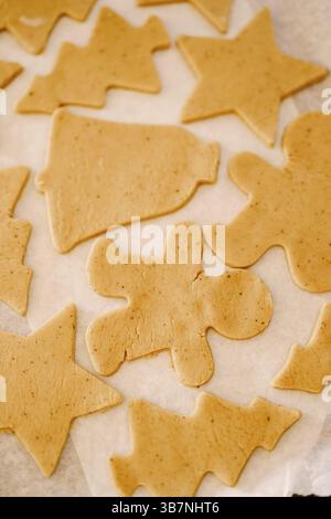 Process of making homemade cookies or gingerbread in different forms. Raw dough cookies lie on a baking sheet covered with parchment for baking before Stock Photo
