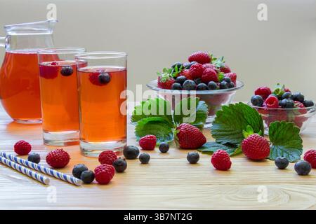 Two glasses filled with a berry beverage sit on a wooden table beside bowls of fresh raspberries and blueberries. Strawberries add a pop of color to the lively arrangement. Stock Photo
