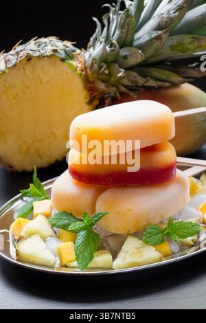 Mango pineapple ice cream stacked on a silver platter is garnished with mint leaves and accompanied by freshly cut fruit. Tropical pineapples add to the vibrant atmosphere. Stock Photo