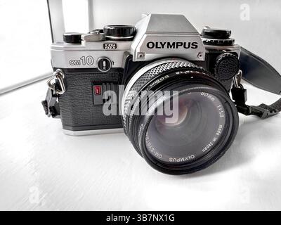 Close-up of a vintage Olympus OM10 film camera with a Zuiko lens set on a white surface near a window Stock Photo