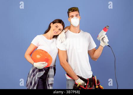 Young couple ready for repair, posing with construction tools over blue background Stock Photo