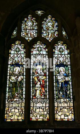 A detailed stained glass window in a church displaying three religious figures with intricate designs and vibrant colors St John the Baptist Devizes Stock Photo