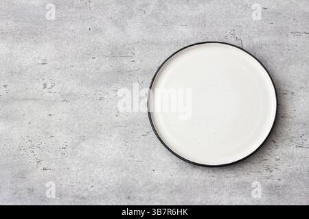 Empty round white ceramic plate with black rim on concrete gray textured background. Minimalist table setting, top view. Ideal for food mockups and de Stock Photo
