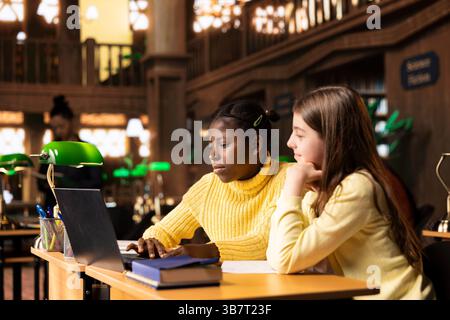 Classmates friends doing a school team project on video call webinar with their teacher, discussing about reliable sources from the library database. Attending an online class on laptop. Stock Photo