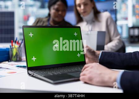 Factory employee works on green screen laptop next to executives discussing solar panel automation strategies. Worker typing on mockup notebook next to team enhancing manufacturing processes, Close up Stock Photo