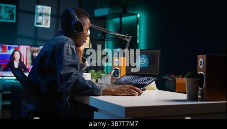 Programmer in living room office typing on keyboard, updating artificial intelligence neural networks, writing binary code scripts. Freelancing system administrator upgrading high tech AI, camera B Stock Photo